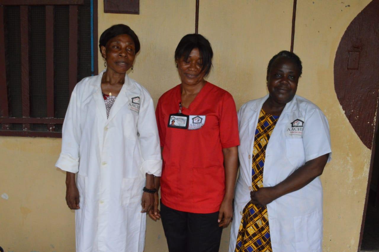 Three women employees stood in a row, two wearing white scrubs and the middle one wearing a red shirt.